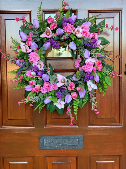 Handmade spring faux flower door wreath in pinks, purples and green.